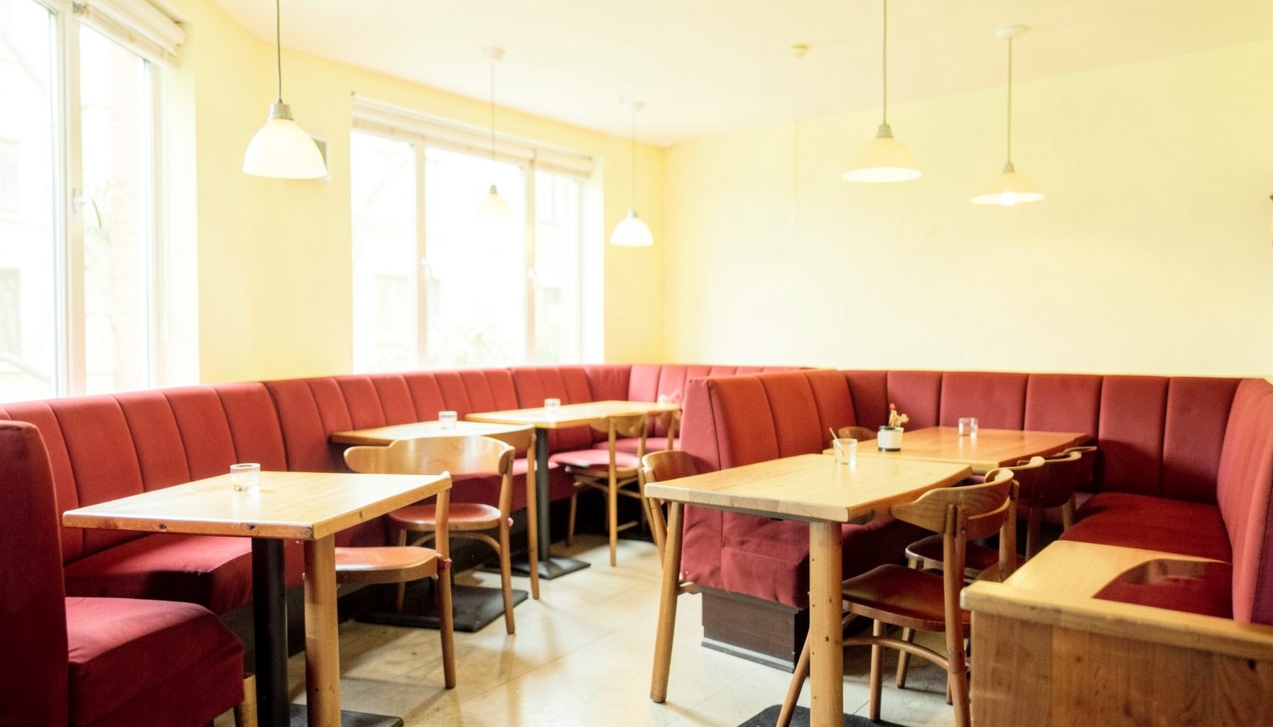 Warm, airy restaurant interior with wood tables, red booth seating, and soft pendant lighting, inviting and relaxed