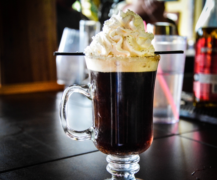 Hot dark coffee drink topped with whipped cream in a glass mug with two straws, dark and cream tones, cozy mood
