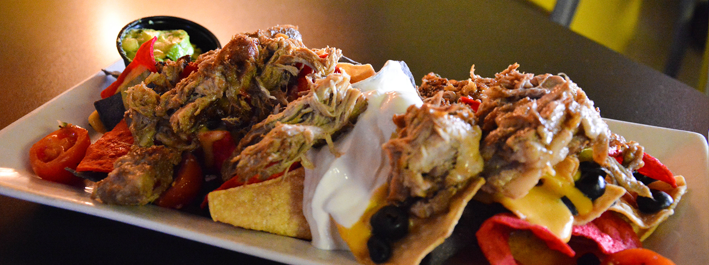 Loaded nachos with shredded meat, melted cheese, sour cream, olives, and colorful tortilla chips with a side of guacamole
